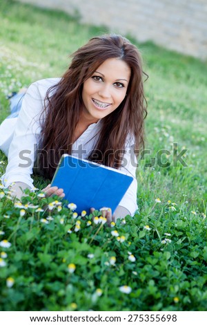 Brunette cool girl with a tablet lying on the grass with many flowers