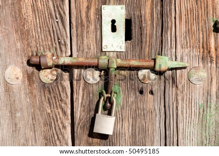 Old wooden door shut with an old rusty lock and padlock