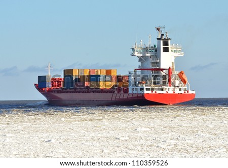 cargo container ship sailing in sea full of ice in winter