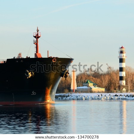 cargo ship\'s bow heading forward against a lighthouse