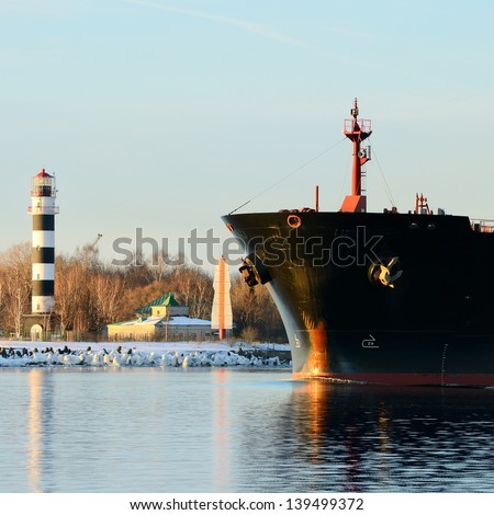 cargo ship's bow heading forward against a lighthouse