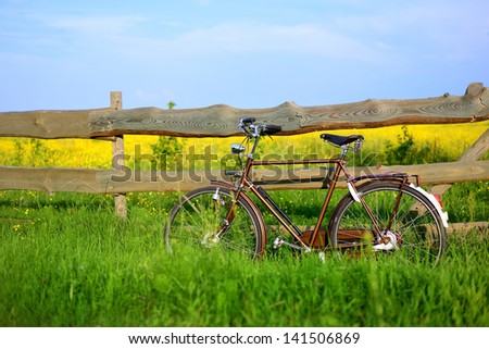Old vintage brown bicycle near the fence of a flower field. Shallow depth of field