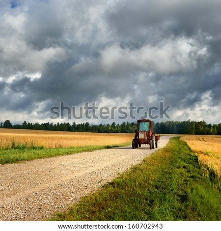 tractor on the road and cereal field against dark stormy clouds