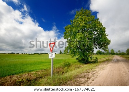 Green field and the road sign on a country road against stormy sky