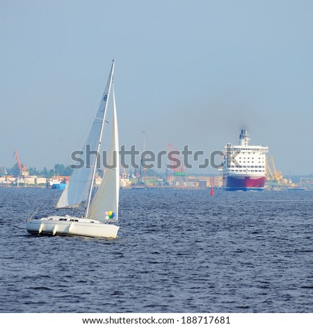 white sail yacht against large black cruise liner ship in port o