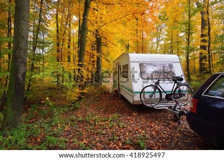 Caravan trailer with bicycle parked in a beautiful beech tree forest in autumn.