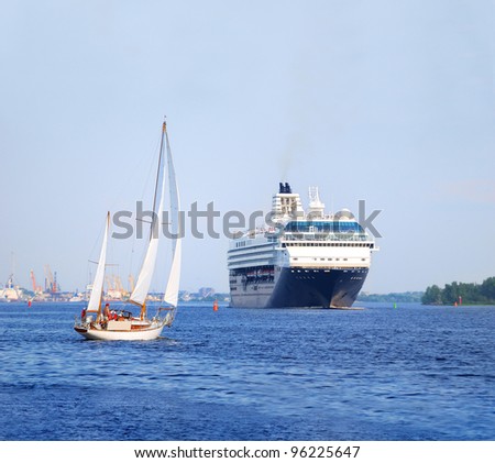 white sail yacht against large black cruise liner ship in port of Riga