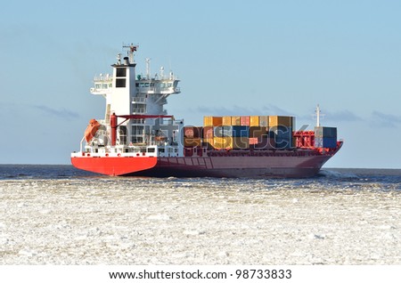 cargo container ship sailing in sea full of ice in winter