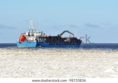 cargo ship loaded with trees sailing in sea full of ice in winter