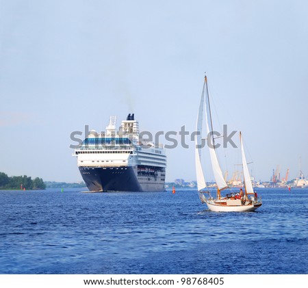 white sail yacht against large black cruise liner ship in port of Riga