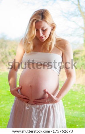 Pregnant woman looking at her belly, spring background, 34 week of pregnancy