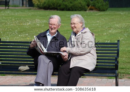 Happy senior couple reading a newspaper on a park bench