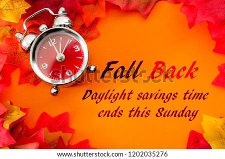 Fall back, the end of daylight savings time and turn clocks back on hour concept with a clock surrounded by dried yellow leaves with the text Fall back, daylight savings time ends this Sunday
