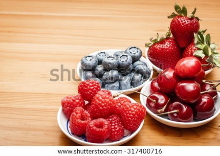Small bowls of fruit containing cherries, strawberries, blueberries and rasberries on a wooden table
