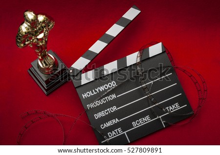 Hollywood film awards concept with shiny metallic movie award wrapped in celluloid film strip on red carpet with clapper board