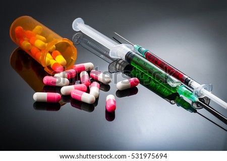 Injectables, doping and medical prescription drugs concept on dark background with white and pink caplets and syringes filled with red and green liquid chemicals