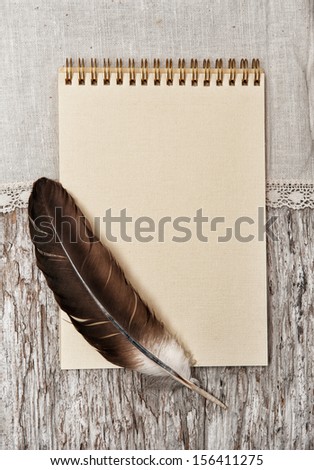 Paper notebook, feather and linen fabric on the old wood