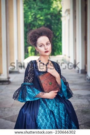 Beautiful young woman in blue medieval dress with book