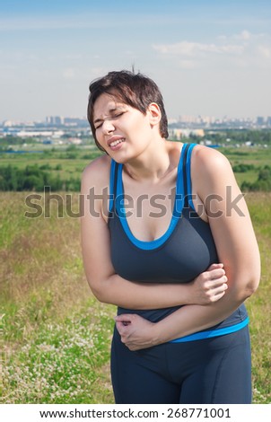 Fitness beautiful plus size woman with pain in her belly outdoor