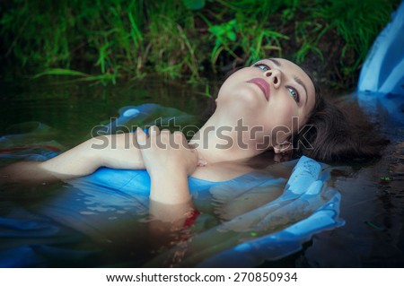 Young beautiful drowned woman in blue dress lying in the water outdoor