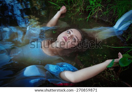 Young beautiful drowned woman in blue dress lying in the water outdoor