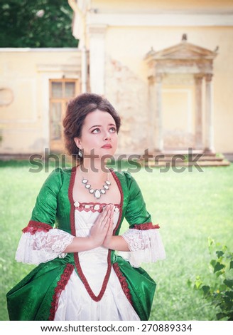 Beautiful young medieval woman in green dress praying outdoor