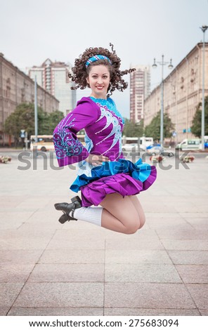 Young beautiful girl in irish dance dress and wig jumping outdoor