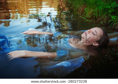 Young beautiful drowned woman in blue dress lying in the water