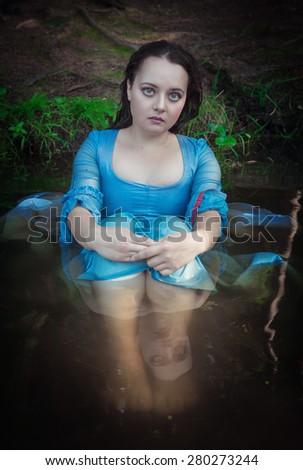 Beautiful young woman with long medieval dress sitting in the water outdoor