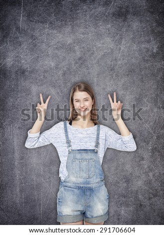 Happy young teenager girl showing victory sign on the chalkboard background