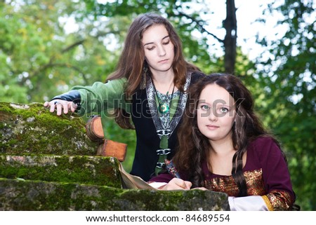 Two young women in medieval dresses writing papers