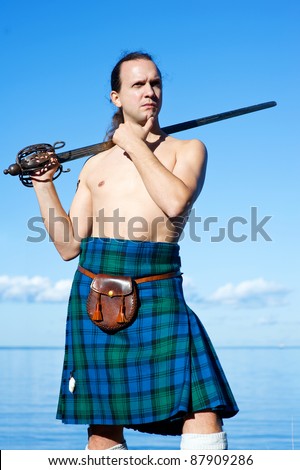 Man with naked torso in kilt on the sky background