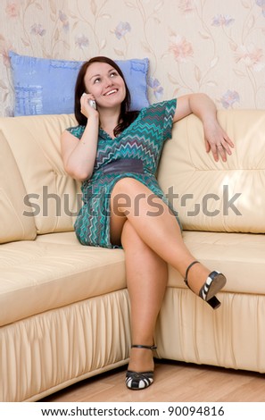Beautiful woman talking on telephone and sitting on the sofa at her home