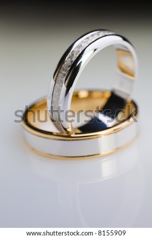 Two white gold engagement rings over a white reflective background