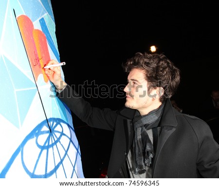 BERLIN - NOVEMBER 12: Orlando Bloom signing a piece of the former Berlin Wall upon his arrival at the Cinema For Peace Green Evening 2010 at the China Club on November 12, 2010 in Berlin, Germany.