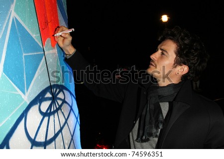 BERLIN - NOVEMBER 12: Orlando Bloom signing a piece of the former Berlin Wall upon his arrival at the Cinema For Peace Green Evening 2010 at the China Club on November 12, 2010 in Berlin, Germany.