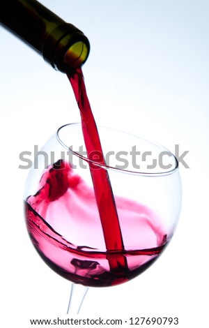 Red wine pouring into wine glass. Studio shot on white background.