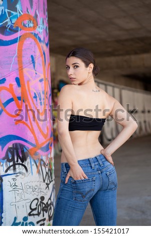Portrait of sexy brunette woman with jeans and black bustier on graffiti wall.