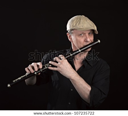 Portrait of a man playing old wooden transverse flute, isolated on black
