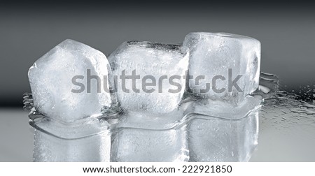 Three ice cubes with reflection on grey gradient background.