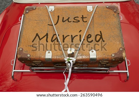 Just Married written on a suitcase placed on the trunk of a red car