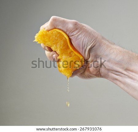 Half Fresh Squeezed Orange Juice by male hand and juice falling with droplets