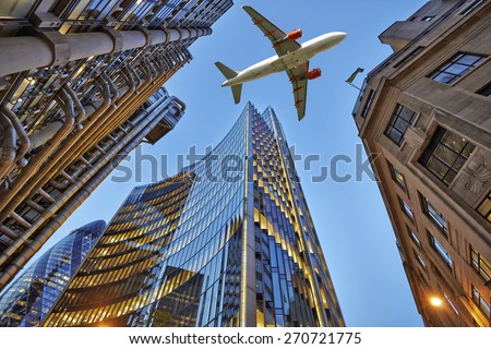 A jet plane flying low over Three different kind of architecture with commercial office buildings exterior. Evening view at bottom skyscrapers.