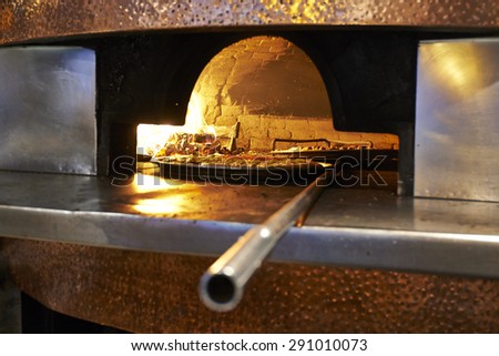 Traditional wood fired pizza being placed into a super hot brick pizza oven.