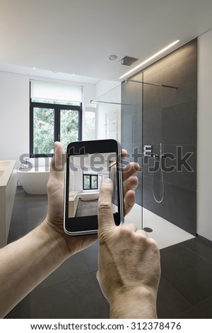 Mobile device with man hands taking picture in  tiled bathroom with windows towards garden, hands on the left side