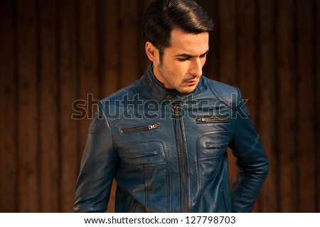 portrait of a young man wearing blue leather jacket against grunge wooden door