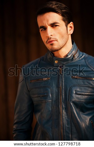 portrait of a young man wearing blue leather jacket against grunge wooden door