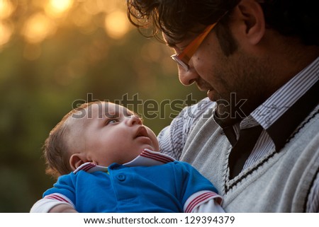 portrait of father and son against nature background, Indian man holding his son in lap.