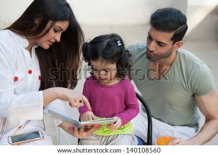 portrait of a multi ethnic family in outdoor, mother and reading a story for her little daughter.