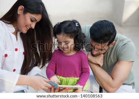 portrait of a multi ethnic family in outdoor, mother and reading a story for her little daughter.